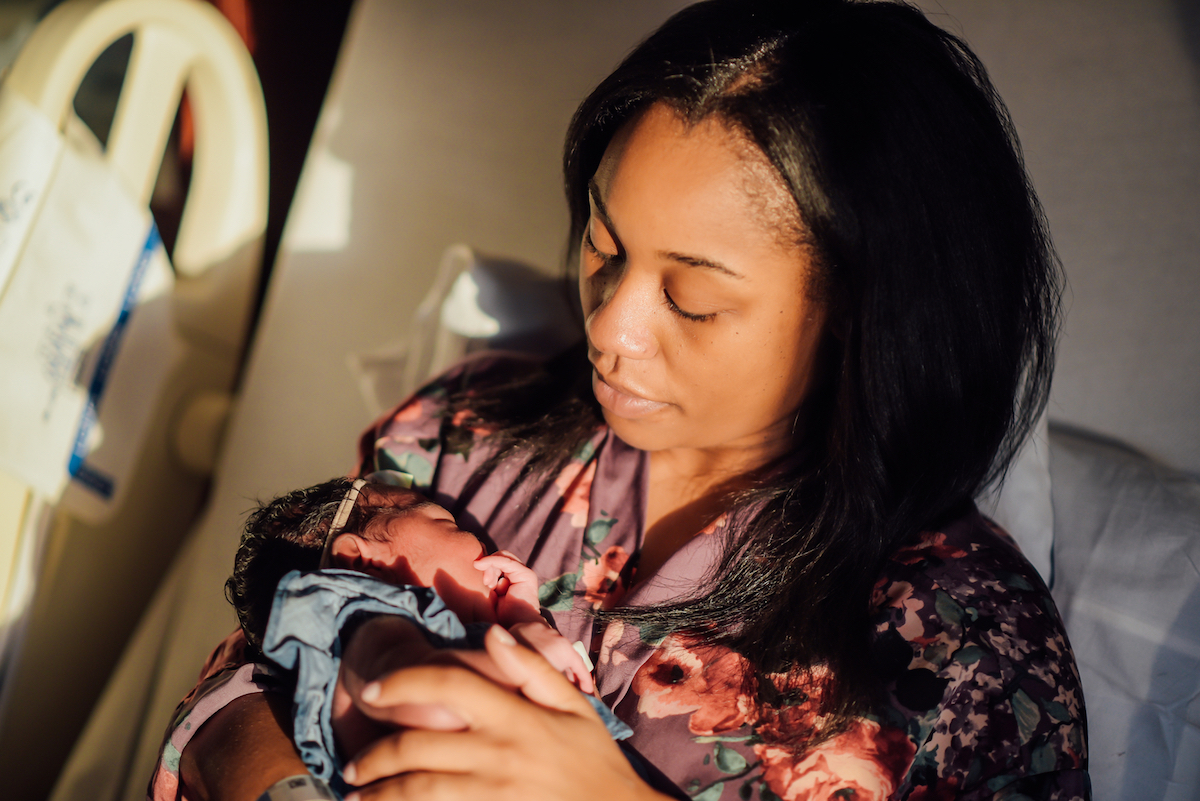 black woman holding newborn baby in hospital bed